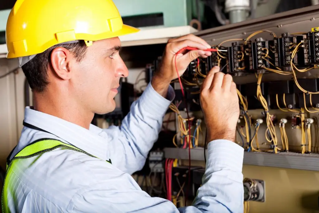 A man in yellow hard hat working on electrical equipment.